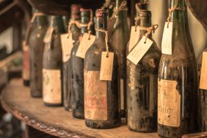 Close-up of old dusty wine bottles with tags on a wooden shelf in a vintage cellar setting.